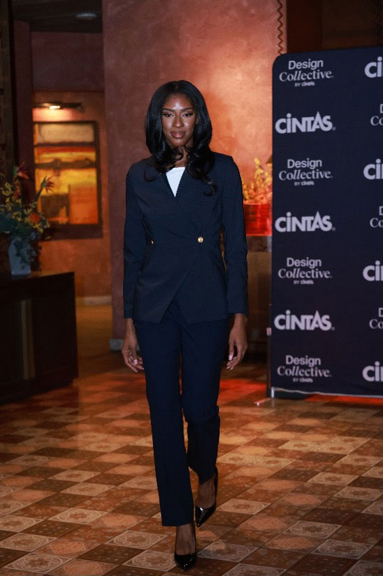 Gaming Fashion Show Article Case Study body image 1 Female model in fitted navy blue pantsuit with gold buttons and white blouse, walking on indoor runway.