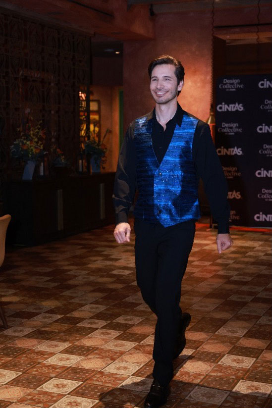 Gaming Fashion Show Article Case Study body image 2 Male model smiling on the catwalk, wearing a black shirt and bright electric blue vest with black pants.